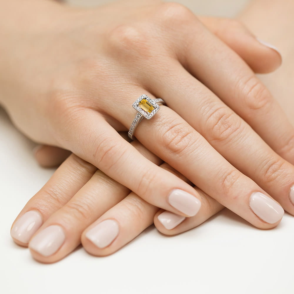 W0422.B3.CIY.01_4 Złoty pierścionek z prostokątnym kamieniem otoczonym diamentami na palcu dłoni.