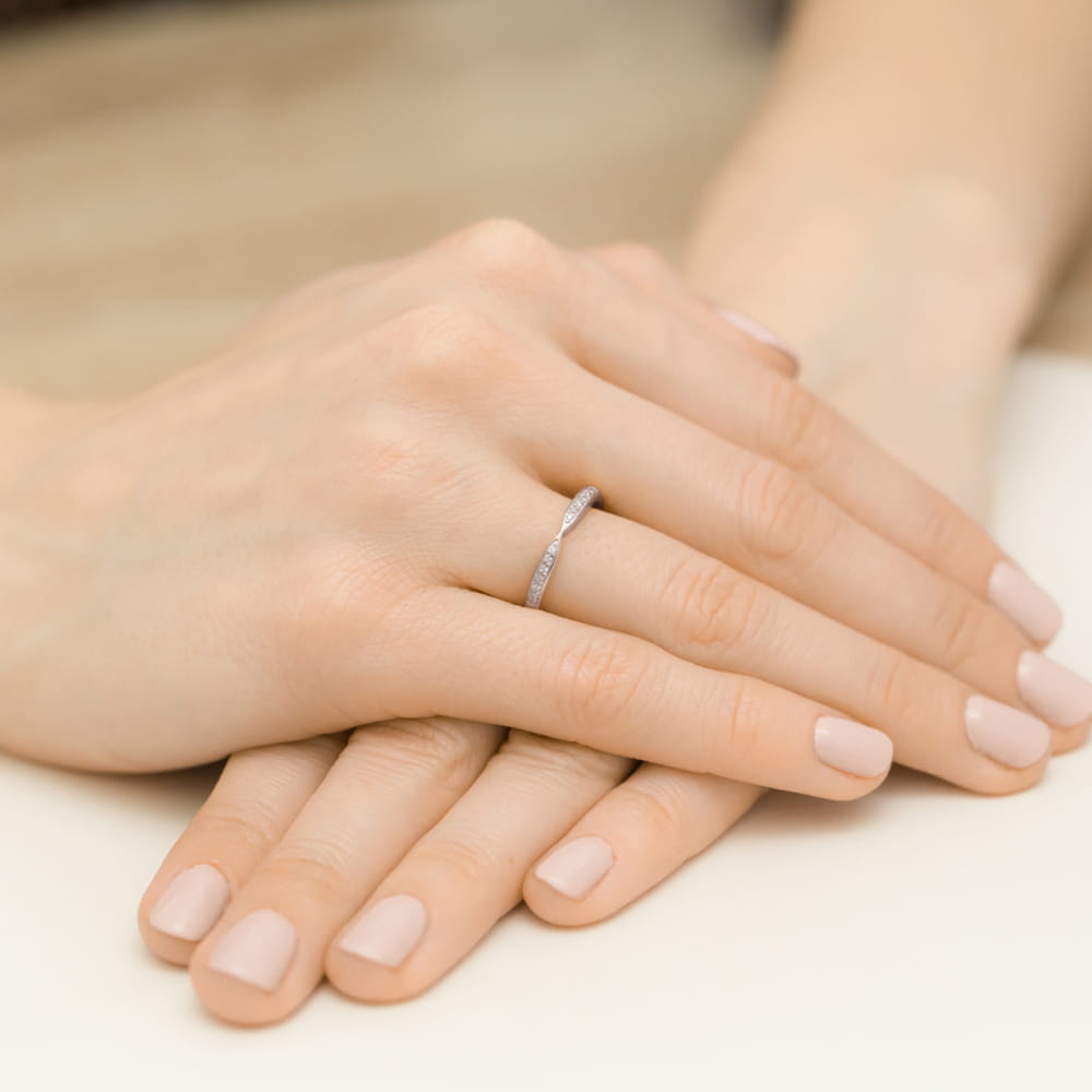W0425.B3.DIW.01_4 Na dłoni z delikatnym manicure znajduje się cienki pierścionek z małymi kamieniami.
