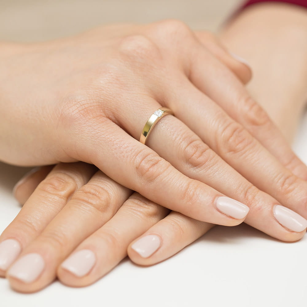 W0432.Z3.DIW.01_4 Dwie dłonie z delikatnym manicure, jedna z nich nosi złoty pierścionek z diamentem.