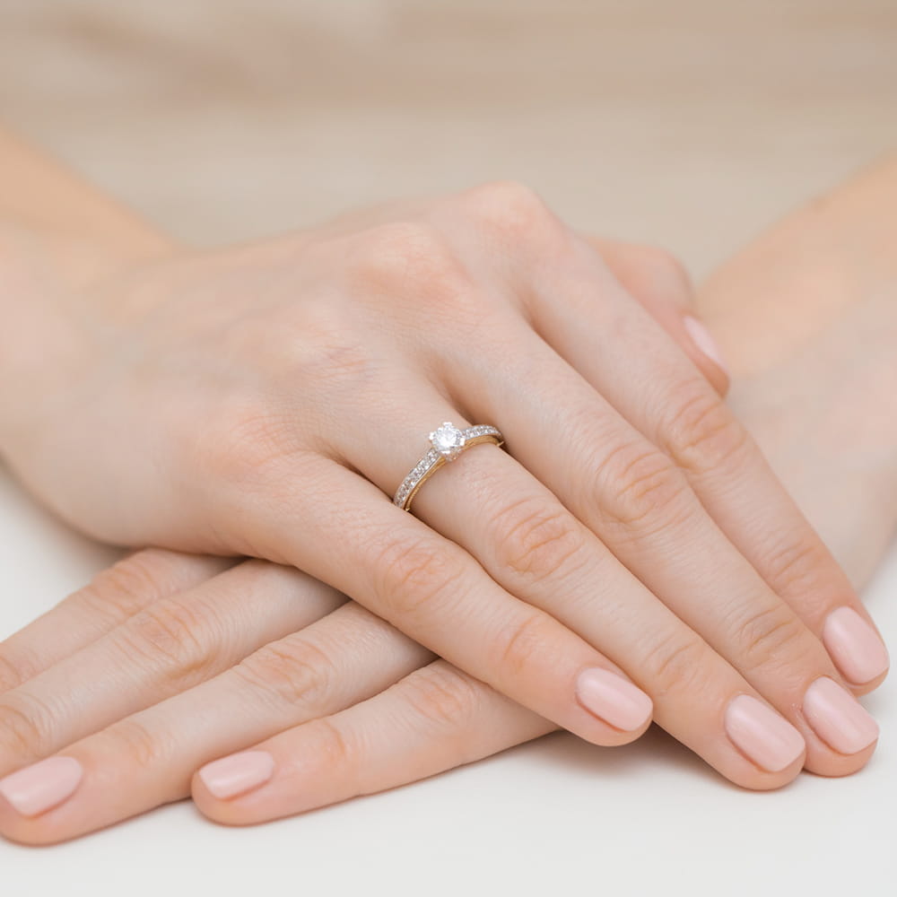 W0439.Z3.DIW.01_4 Dwie dłonie z delikatnym manicure, jedna z pierścionkiem z diamentem na złotej obrączce.