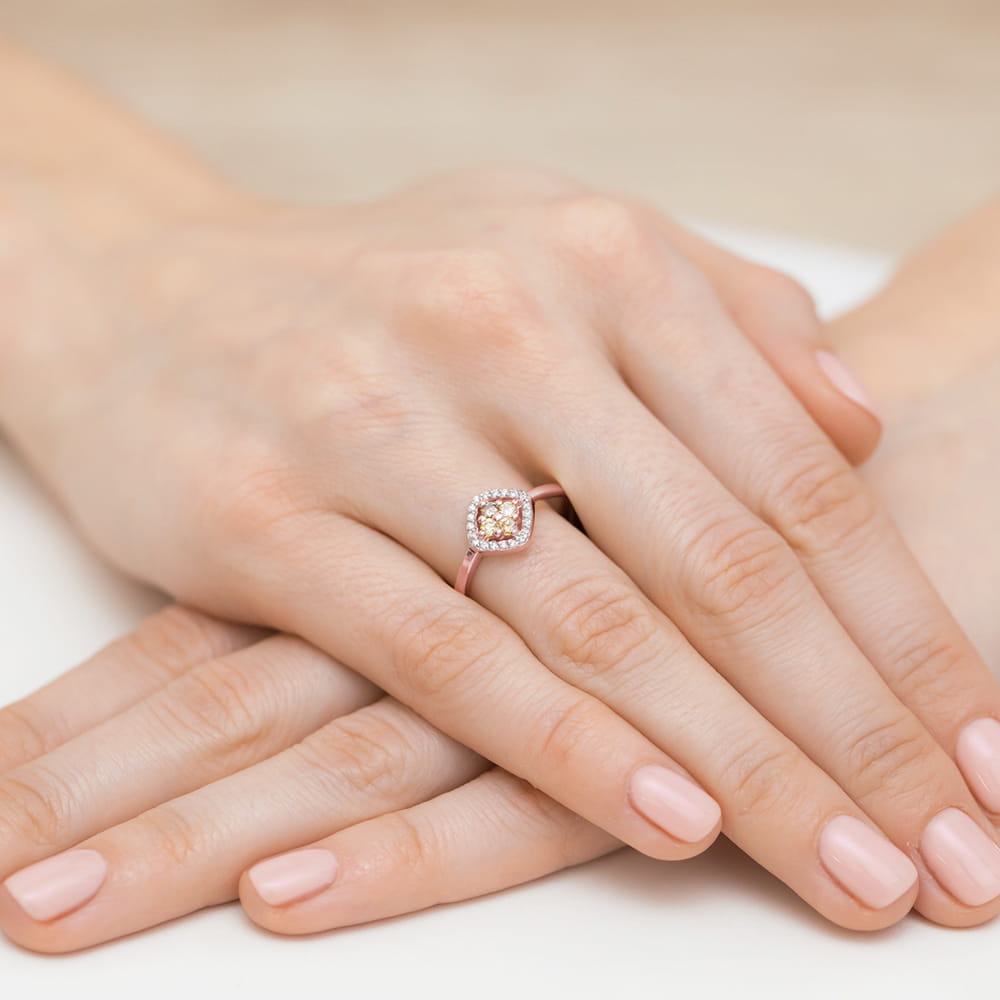 W0441.R3.XXX.01_4 Na dłoni z delikatnym manicure znajduje się pierścionek z centralnym kamieniem otoczonym małymi diamentami.