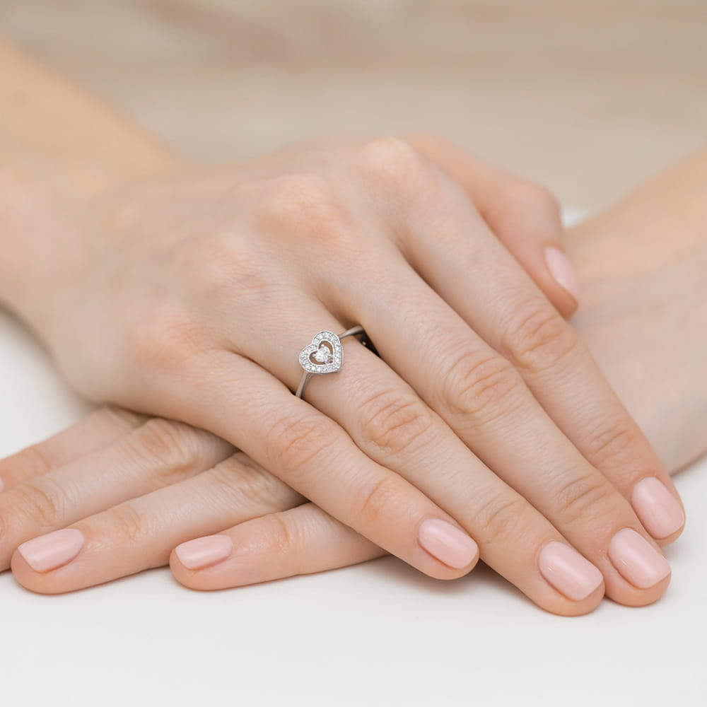 W0442.B3.DIW.01_4 Dwie dłonie z delikatnym manicure, na jednej z nich pierścionek w kształcie serca z diamentami.