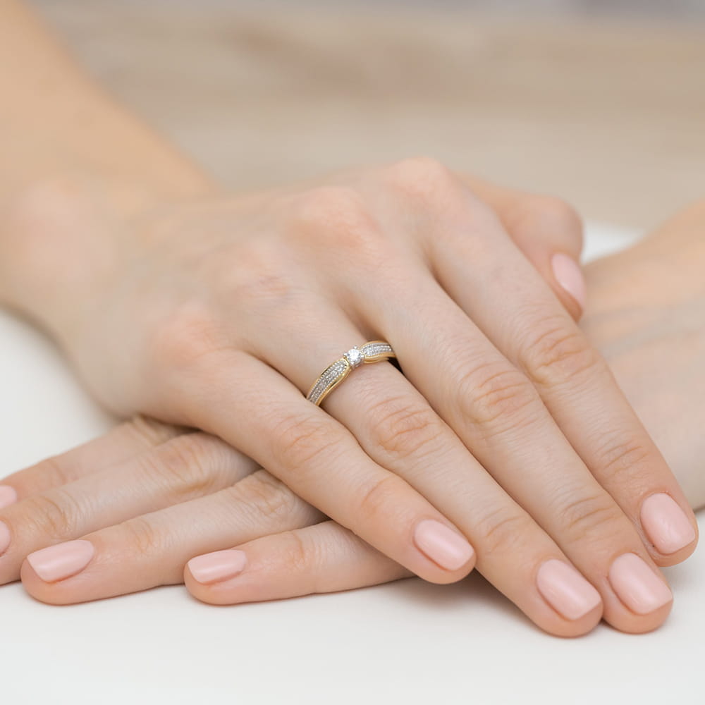 W0449.Z3.DIW.01_4 Dwie ręce z delikatnym pierścionkiem na palcu, z różowymi paznokciami.