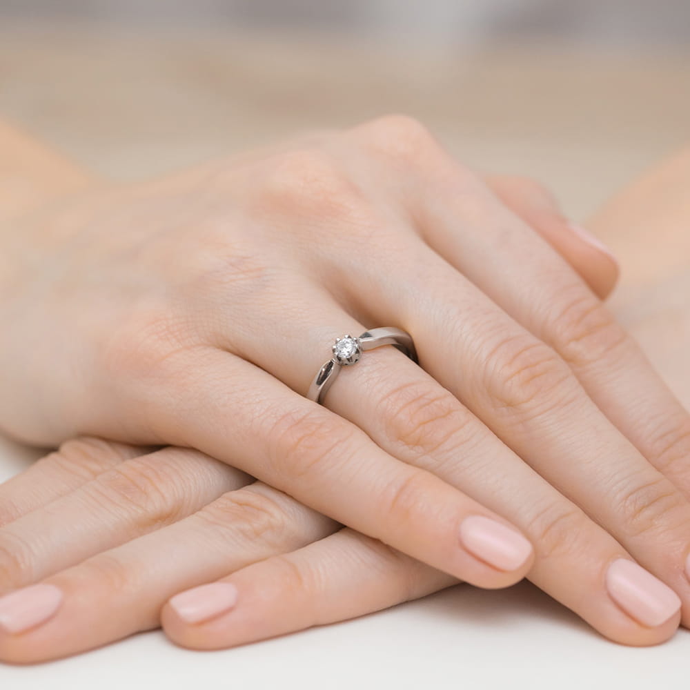W0450.B3.DIW.02_4 Na dłoni z delikatnym manicure znajduje się srebrny pierścionek z dużym, błyszczącym kamieniem.
