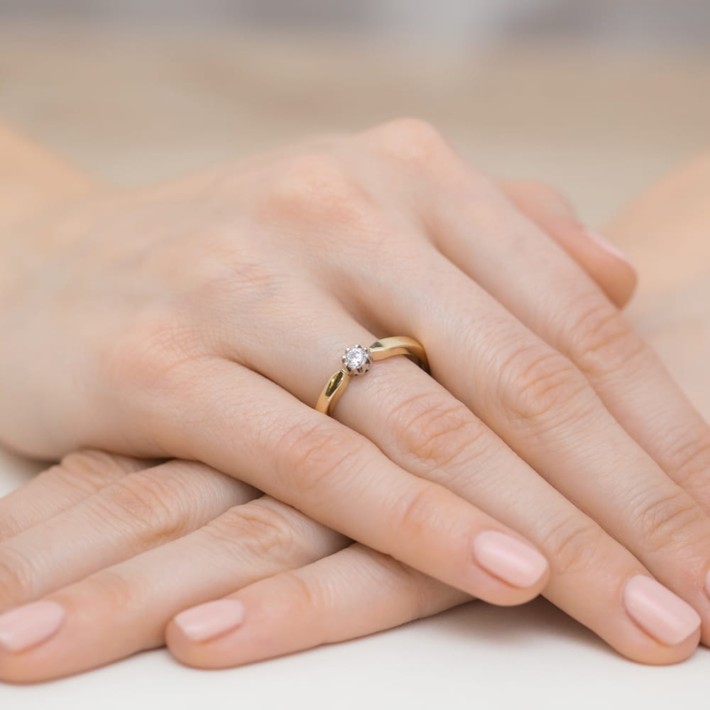 W0450.Z3.DIW.02_4 Złoty pierścionek z diamentem na palcu, dłonie z delikatnym manicure w jasnym kolorze.