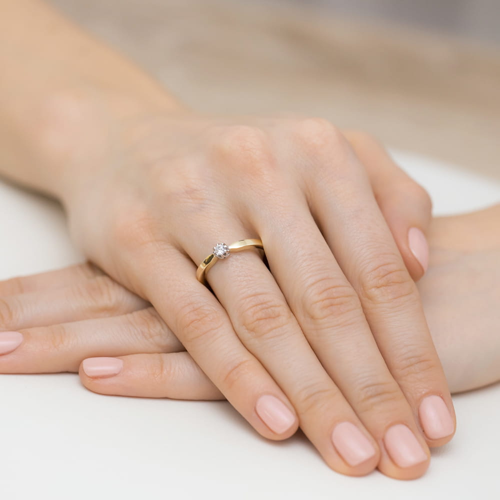 W0450.Z3.DIW.03_4 Złoty pierścionek z diamentem na palcu kobiecej ręki, z delikatnym manicure.
