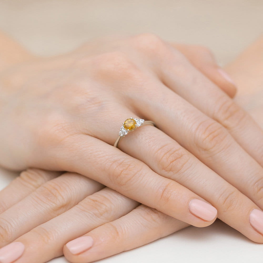 W0451.B3.CIY.01_4 Pierścionek z żółtym kamieniem i diamentami na delikatnej, srebrnej obrączce, na tle dłoni z różowym manicure.