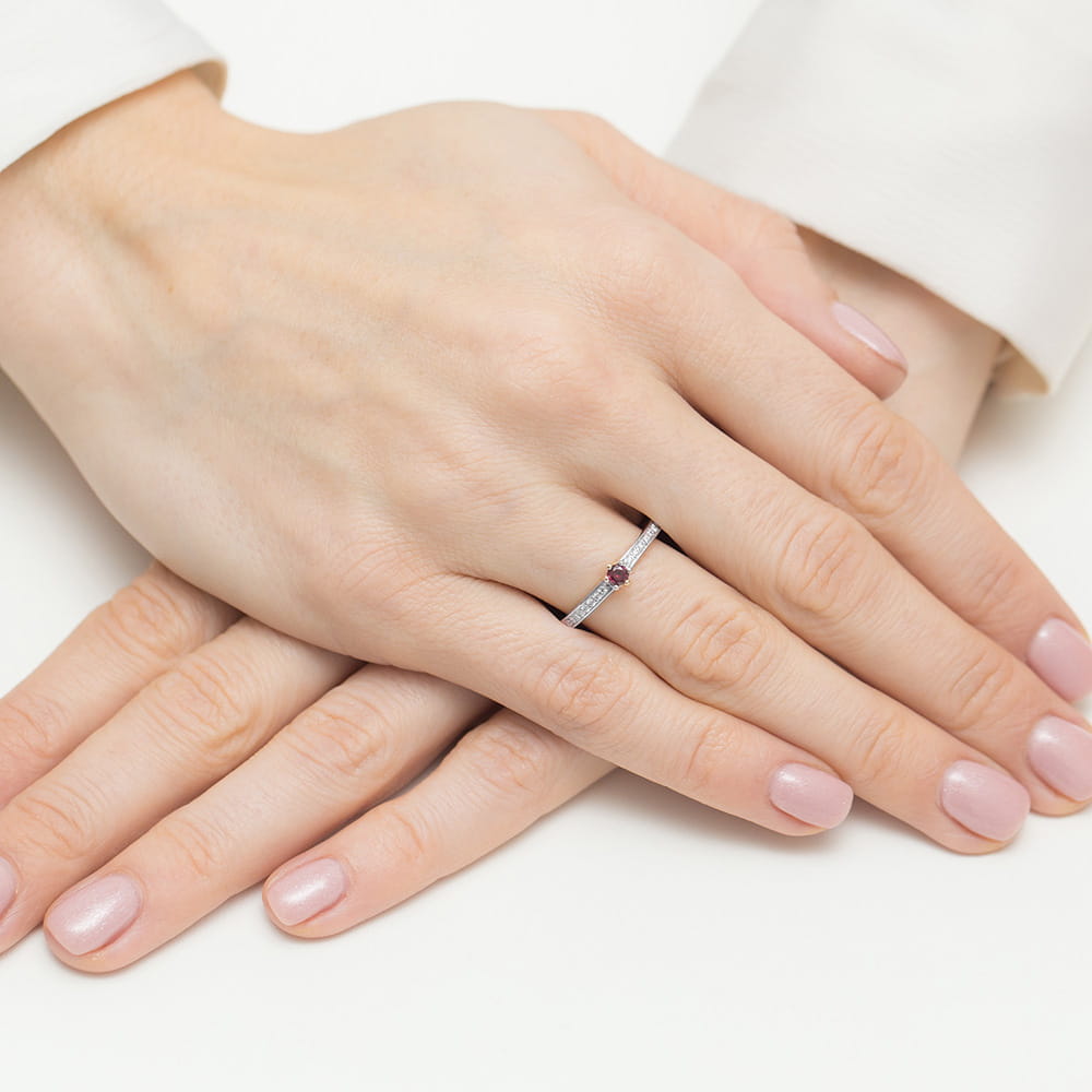 W0459.B3.RUR.01_4 Na dłoni z delikatnym manicure znajduje się cienki pierścionek z małym kamieniem szlachetnym.