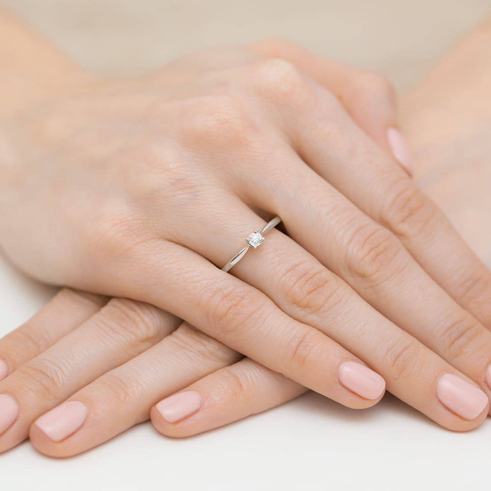 W0461.B3.DIW.02_4 Na dłoni z różowym manicure znajduje się delikatny pierścionek z diamentem.