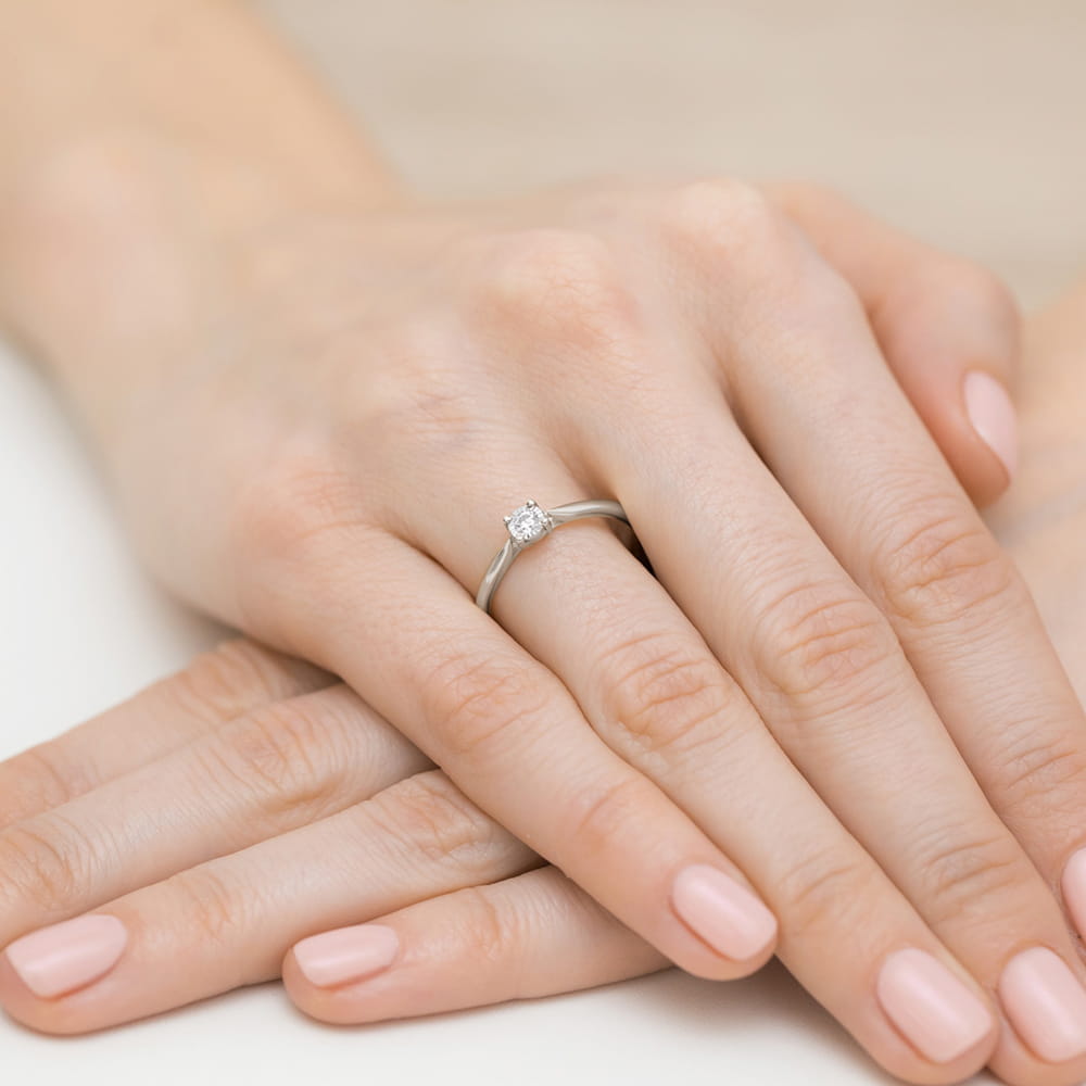 W0461.B3.DIW.03_4 Na dłoni widać srebrny pierścionek z diamentem, otoczony delikatnymi, zadbanymi palcami.