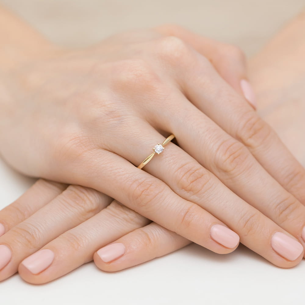 W0461.Z3.DIW.02_4 Złoty pierścionek z diamentem na palcu kobiety, z delikatnie pomalowanymi paznokciami.