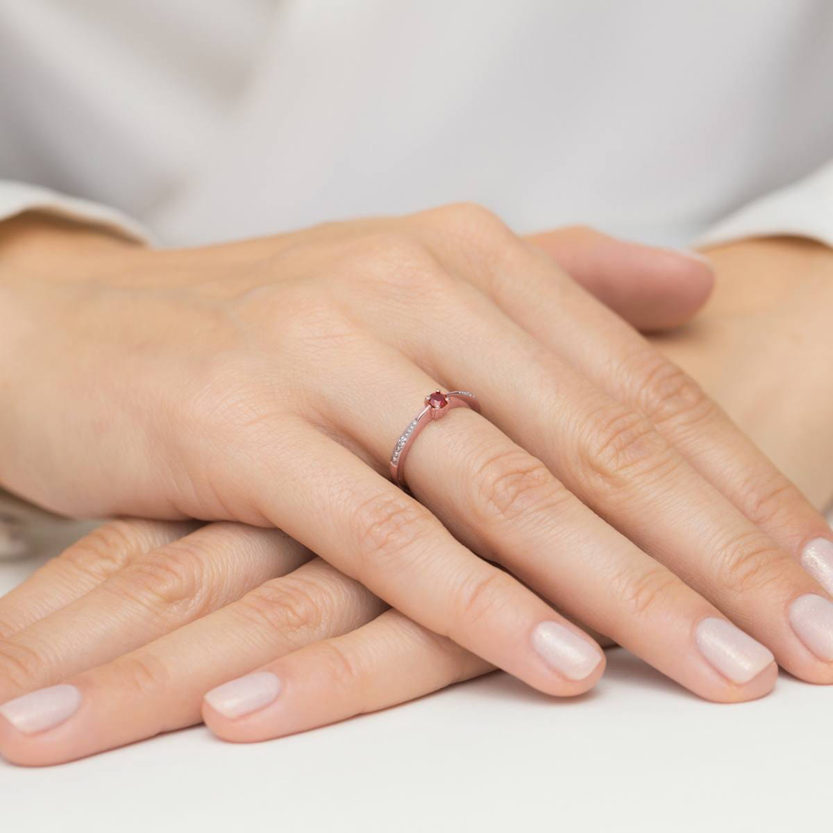 W0465.R3.RUR.01_4 Różowa pierścionek z diamentami na palcu, dłonie z zadbanymi paznokciami na jasnym tle.