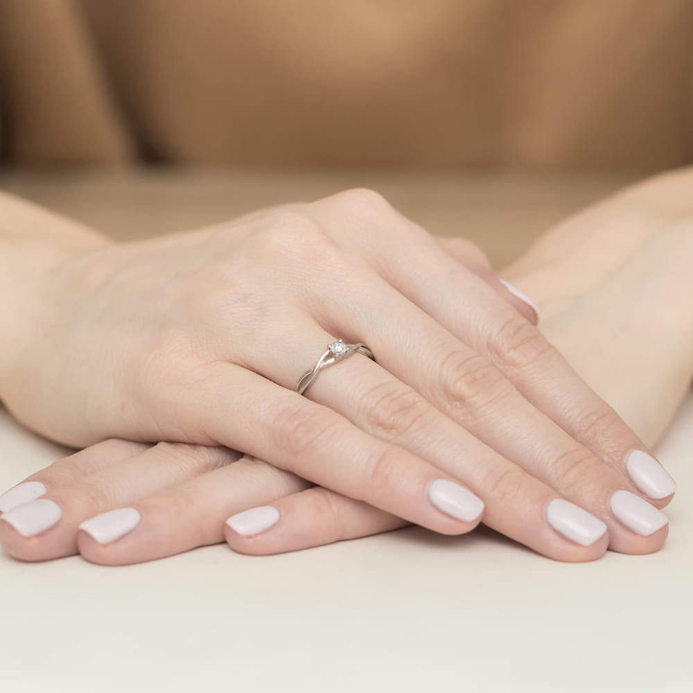 W0470.B3.DIW.01_4 Dwie dłonie z delikatnym pierścionkiem na palcu, z paznokciami pomalowanymi na jasny kolor.