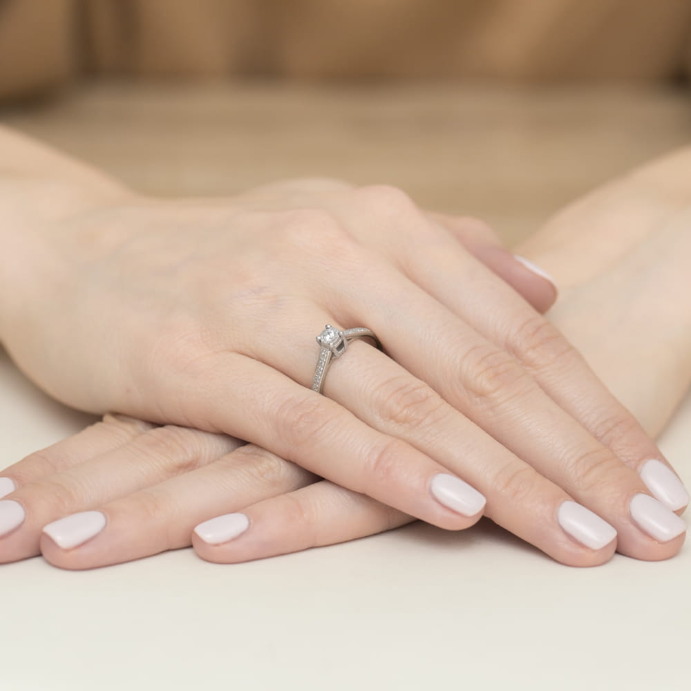 W0474.B3.DIW.01_4 Dwie ręce z delikatnym pierścionkiem na palcu, z zadbanymi paznokciami w jasnym kolorze.