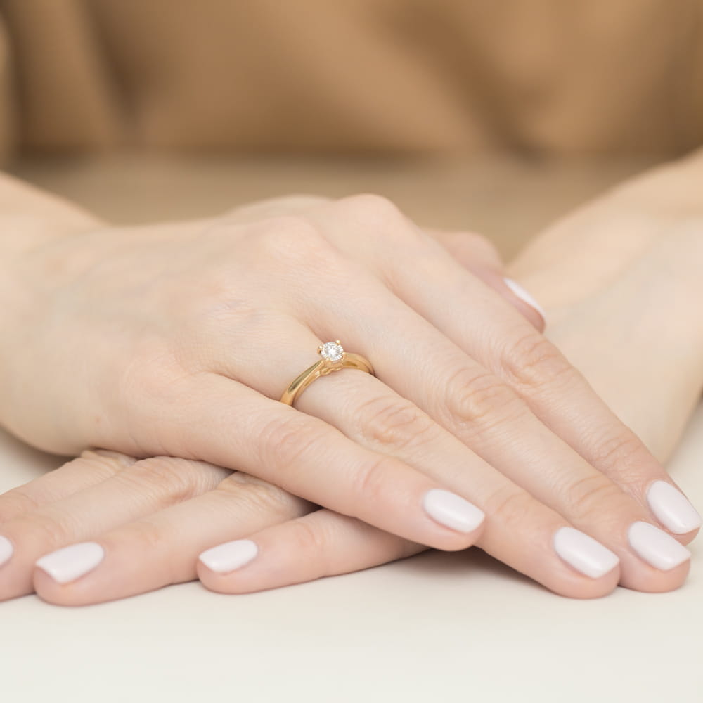 W0475.Z3.DIW.01_4 Złoty pierścionek z diamentem na palcu, dłonie z delikatnym manicure w jasnym kolorze.