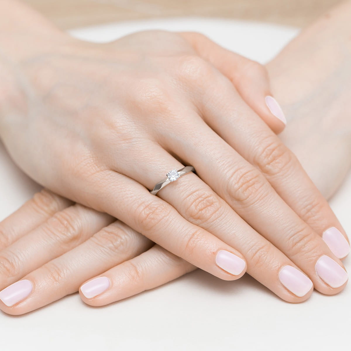 W0484.B3.DIW.03_4 Dwie dłonie z delikatnym manicure, na jednej z nich srebrny pierścionek z diamentem.