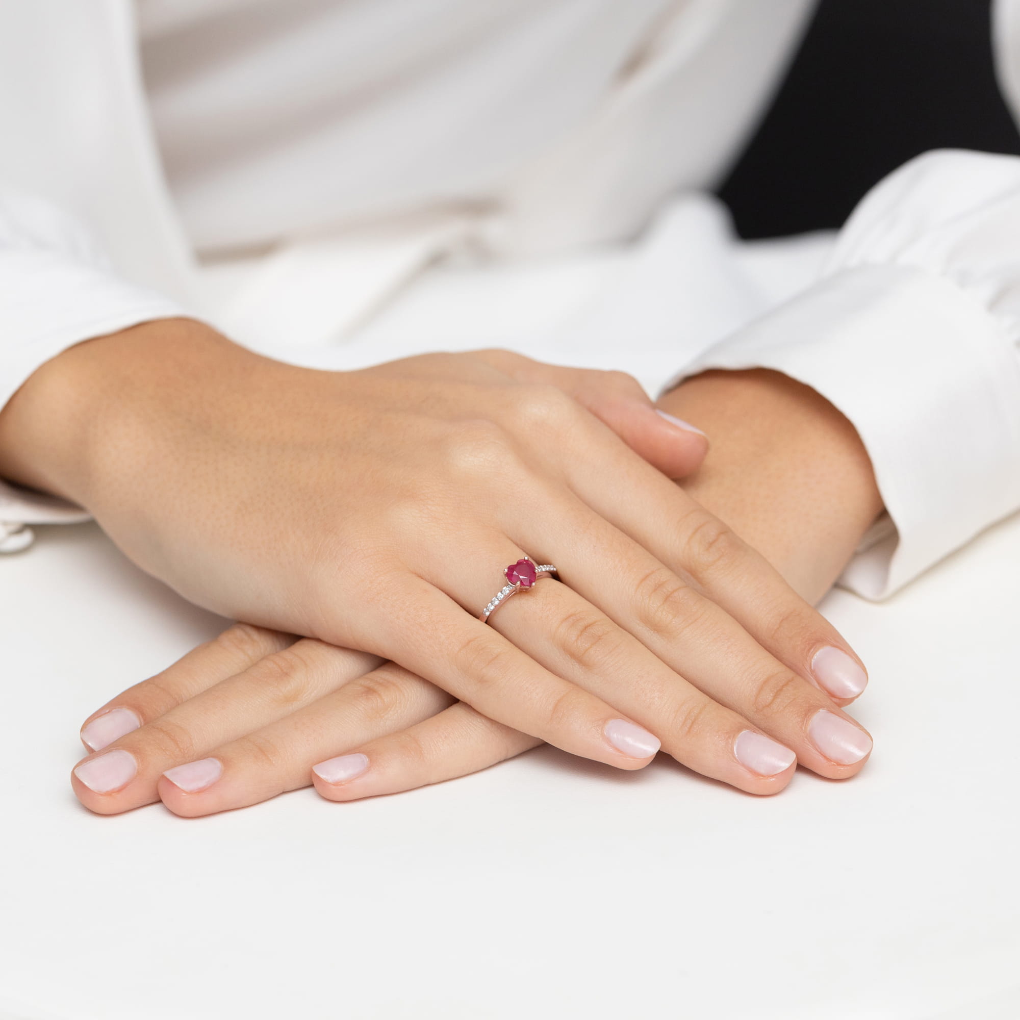 W0486.R3.RUR.01_6 Na dłoni z delikatnym manicure znajduje się pierścionek z czerwonym kamieniem i drobnymi diamentami.