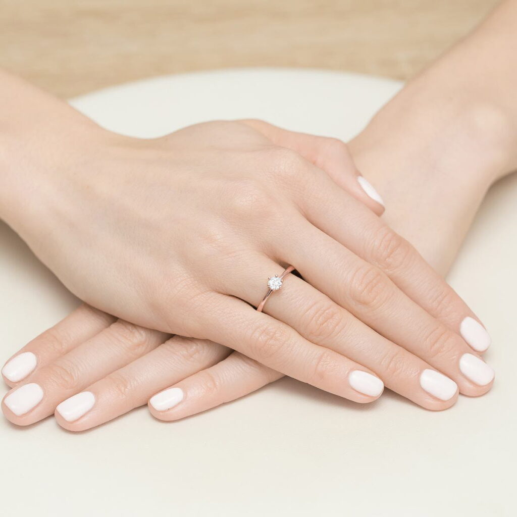 Dwie ręce z białym manicure, jedna z pierścionkiem z diamentem na palcu.