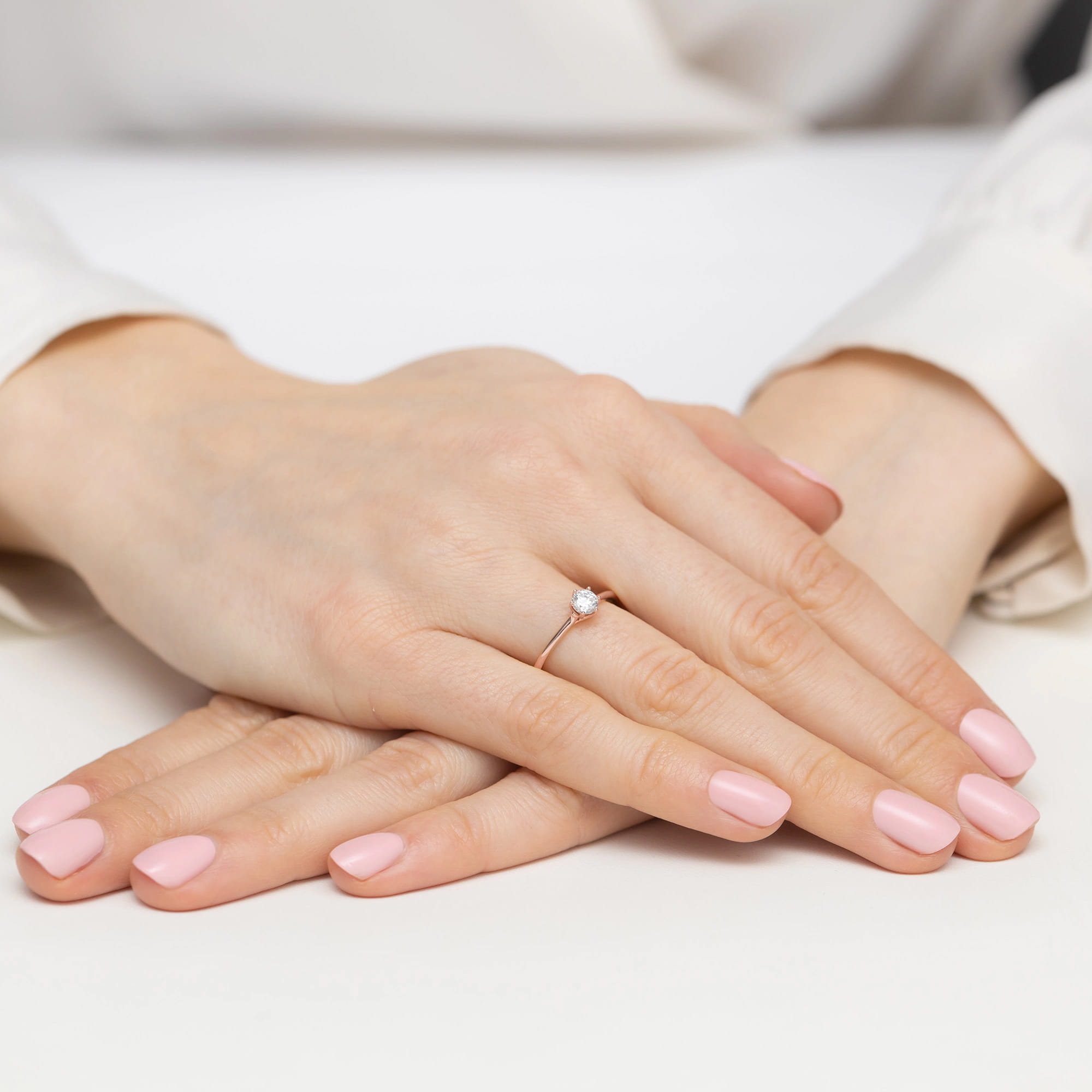 W0499.R3.DIW.02_4 Dwie ręce z różowym manicure, jedna z pierścionkiem z diamentem, ułożone na białym tle.