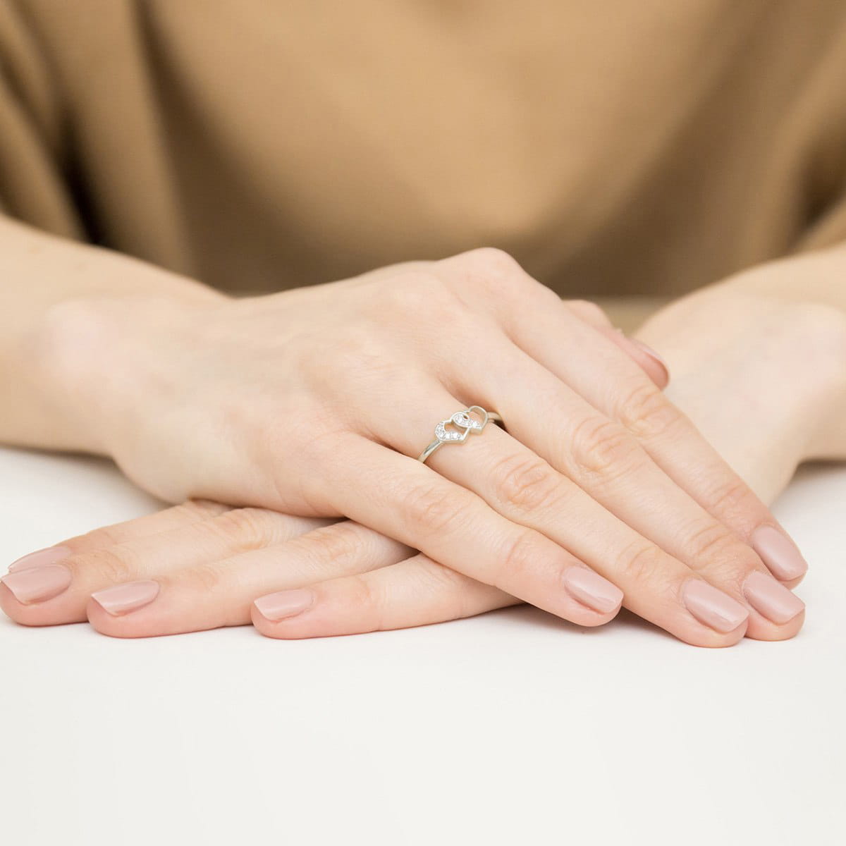 W0500.B3.DIW.01_4 Dwie ręce z delikatnym pierścionkiem na palcu, z zadbanymi paznokciami w jasnym kolorze.