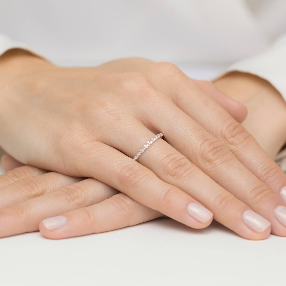 W0504.R3.DIW.01_4 Na dłoni widać delikatny pierścionek z małymi, błyszczącymi kamieniami, otoczony gładkimi palcami.