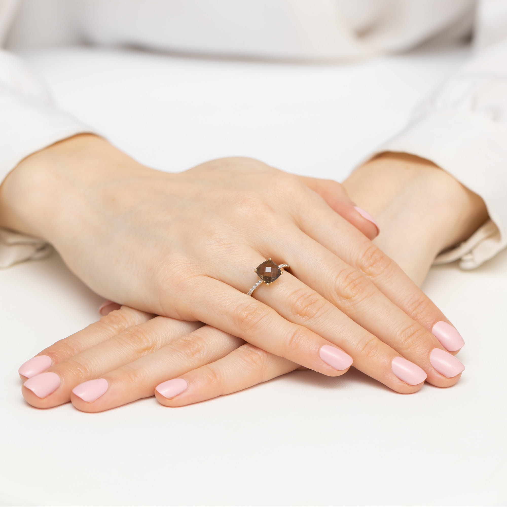 W0511.Z3.QUS.01_4 Dwie ręce z różowym manicure, jedna z pierścionkiem w złotej oprawie, spoczywają na białym tle.