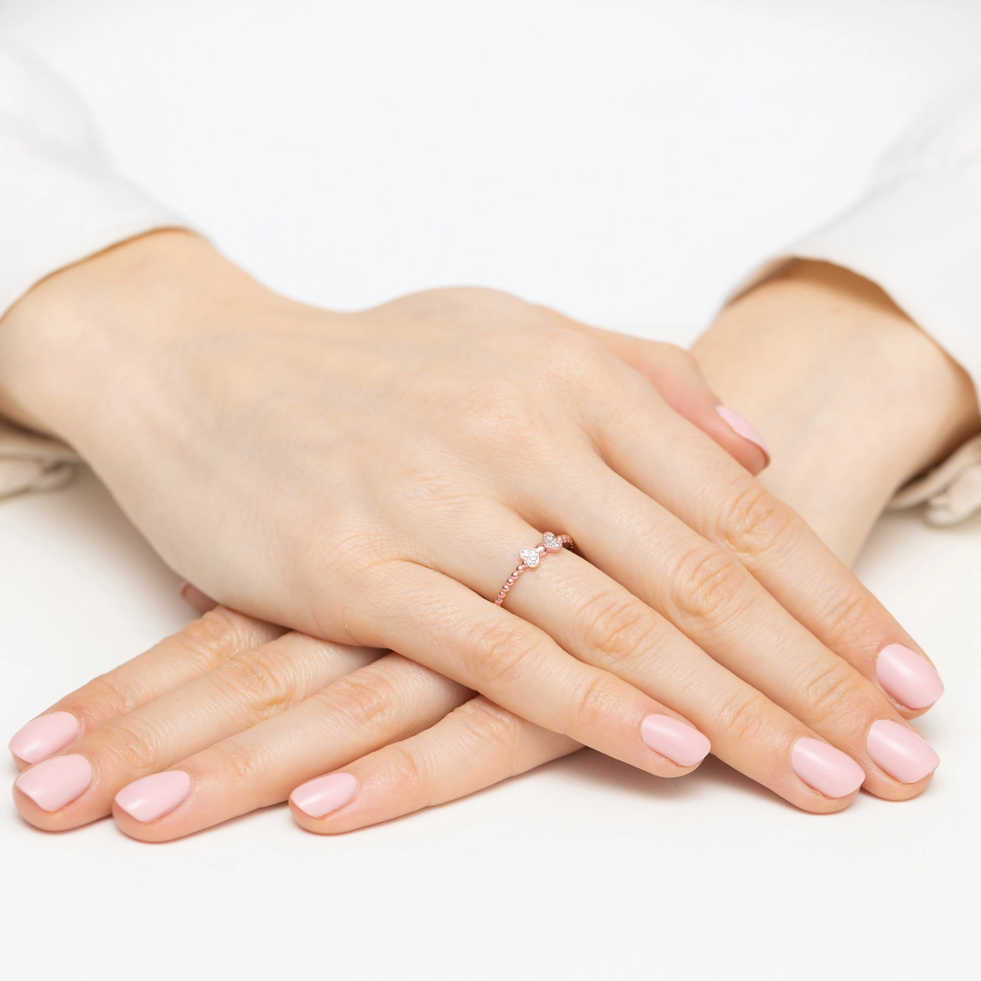 W0523.R3.DIW.01_4 Dwie ręce z różowym manicure, jedna z pierścionkiem z kamieniami, ułożone na białym tle.