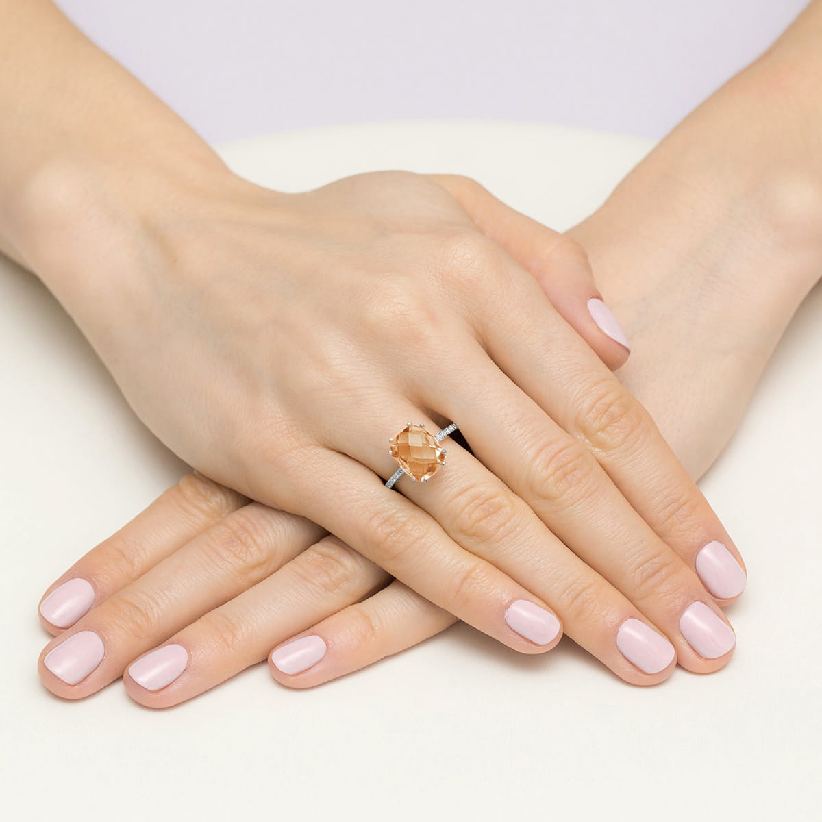 W0527.Z3.MOP.01_4 Na dłoniach z delikatnym manicure znajduje się pierścionek z dużym, pomarańczowym kamieniem.