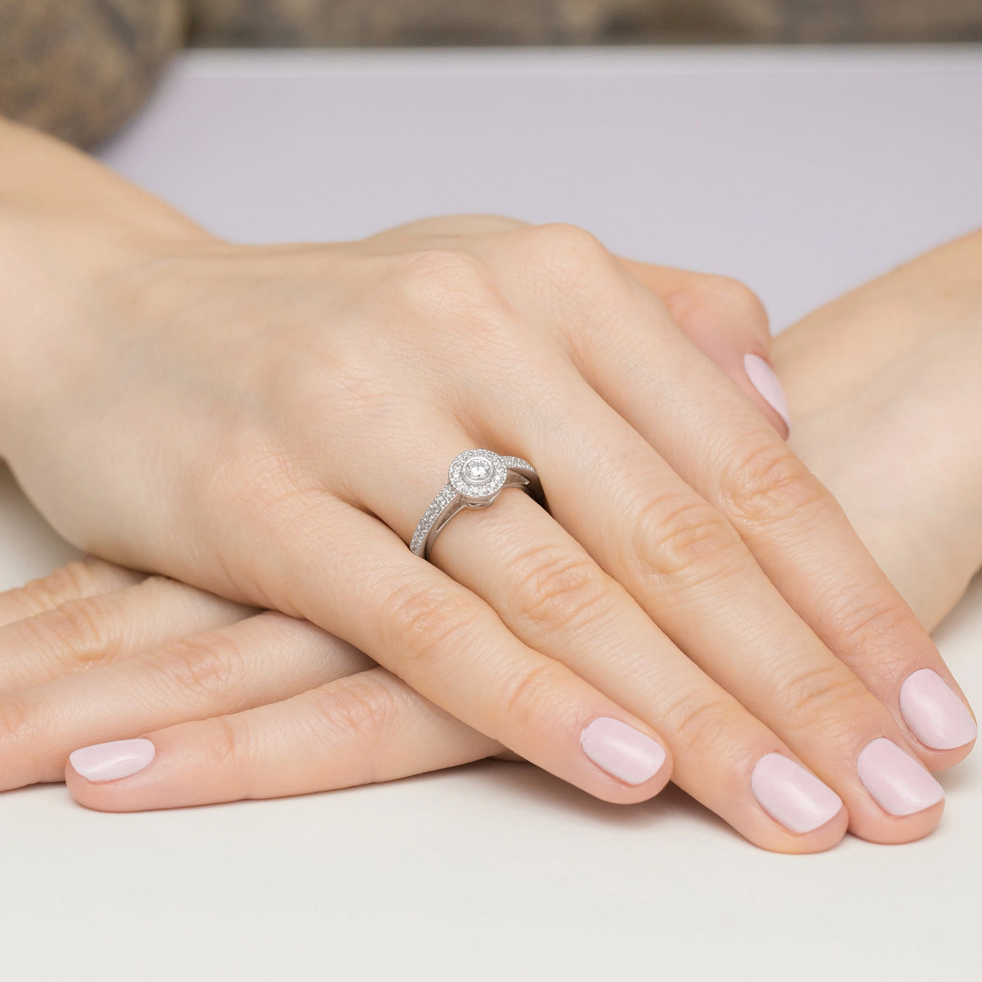 W0530.B3.DIW.01_4 Na dłoni z delikatnym manicure znajduje się pierścionek z okrągłym diamentem i zdobioną obrączką.