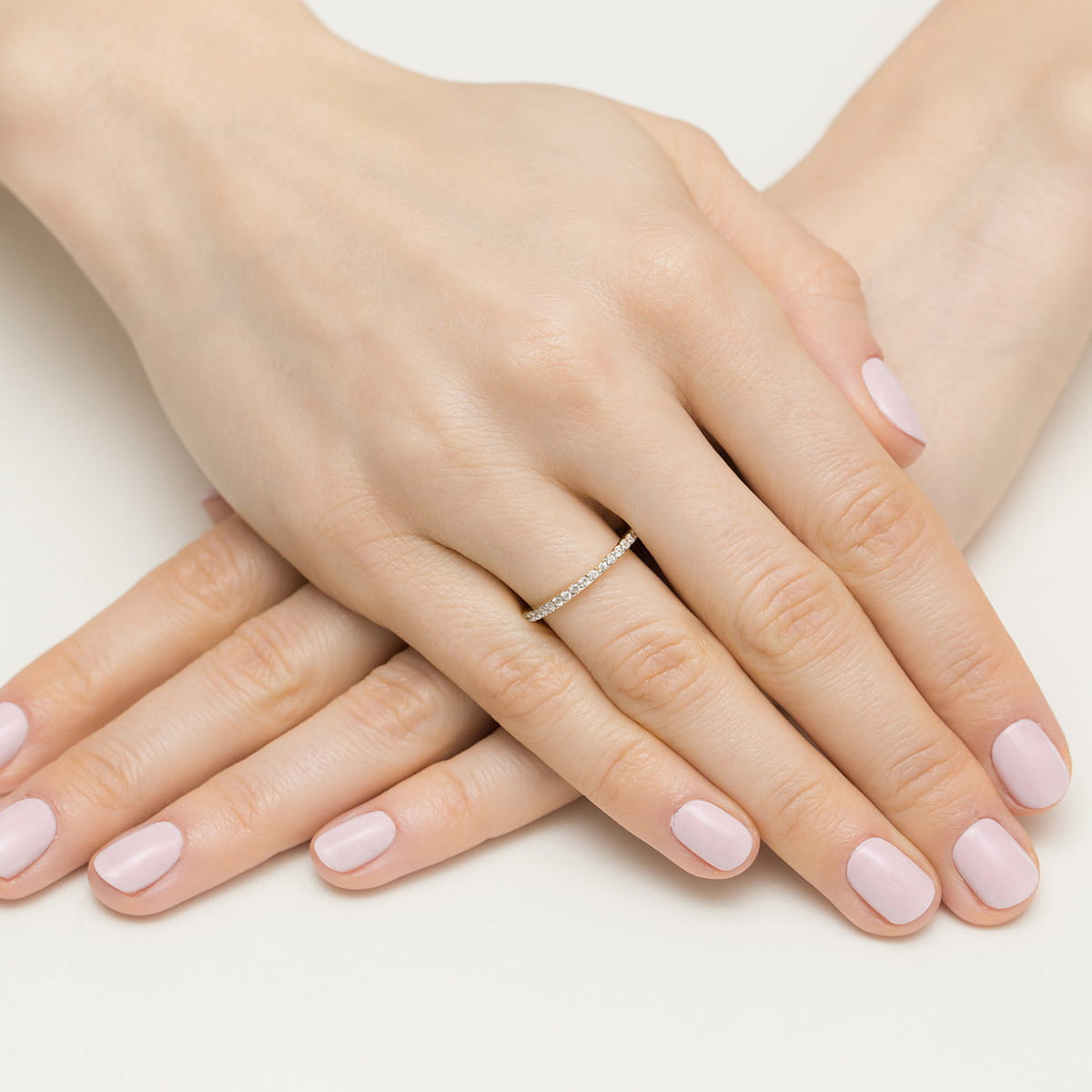 W0531.Z3.LDW.01_4 Dwie ręce z delikatnym pierścionkiem i różowym manicure, ułożone na jasnym tle.