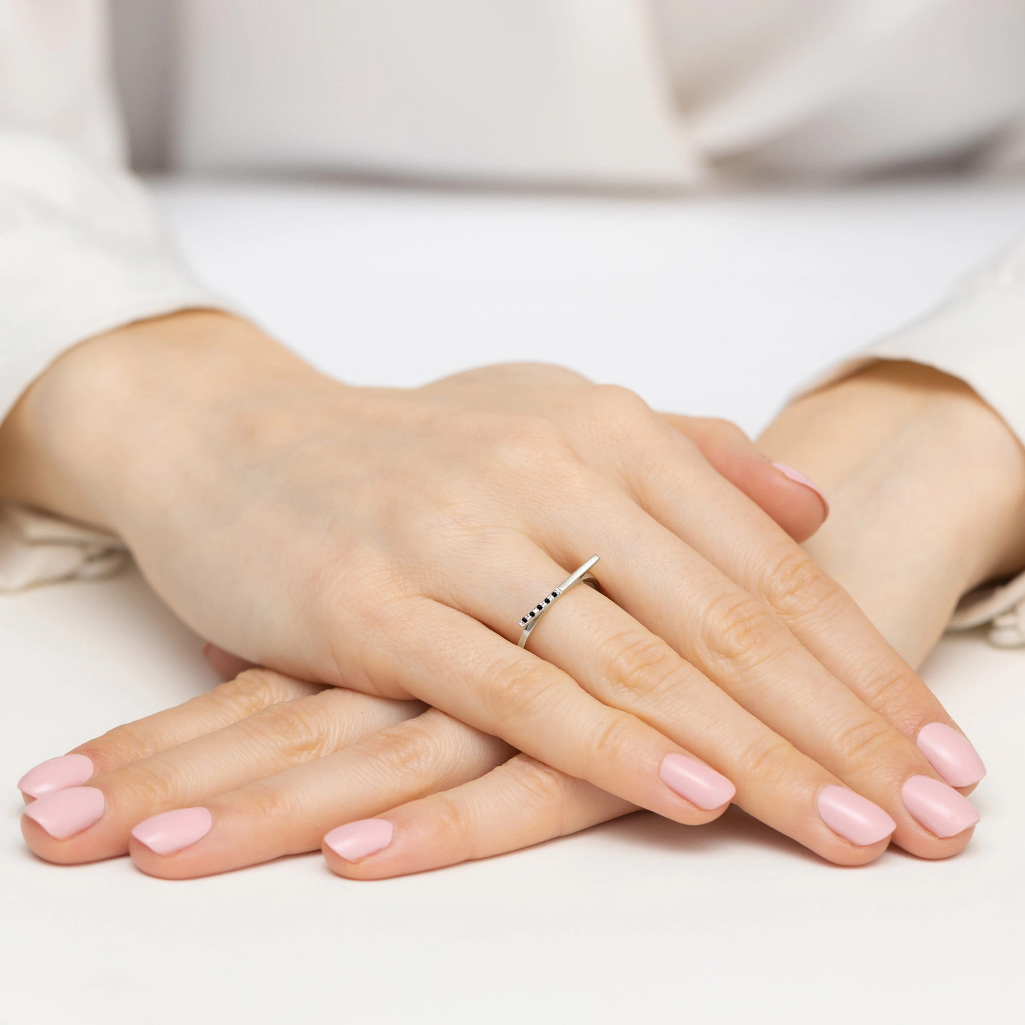 W0537.B3.DIB.01_3 Dwie ręce z delikatnym pierścionkiem i różowym manicure, ułożone na białym tle.