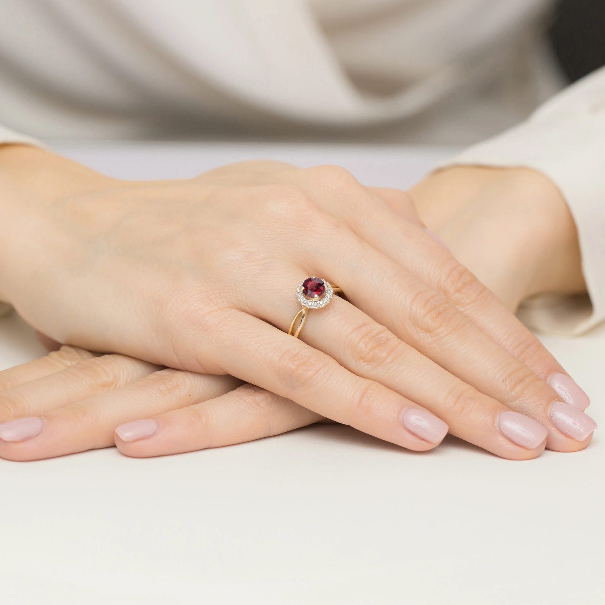 W0538.Z3.RUR.01_4 Zbliżenie na dłoń z pierścionkiem z rubinem i diamentami, na tle jasnego stołu.