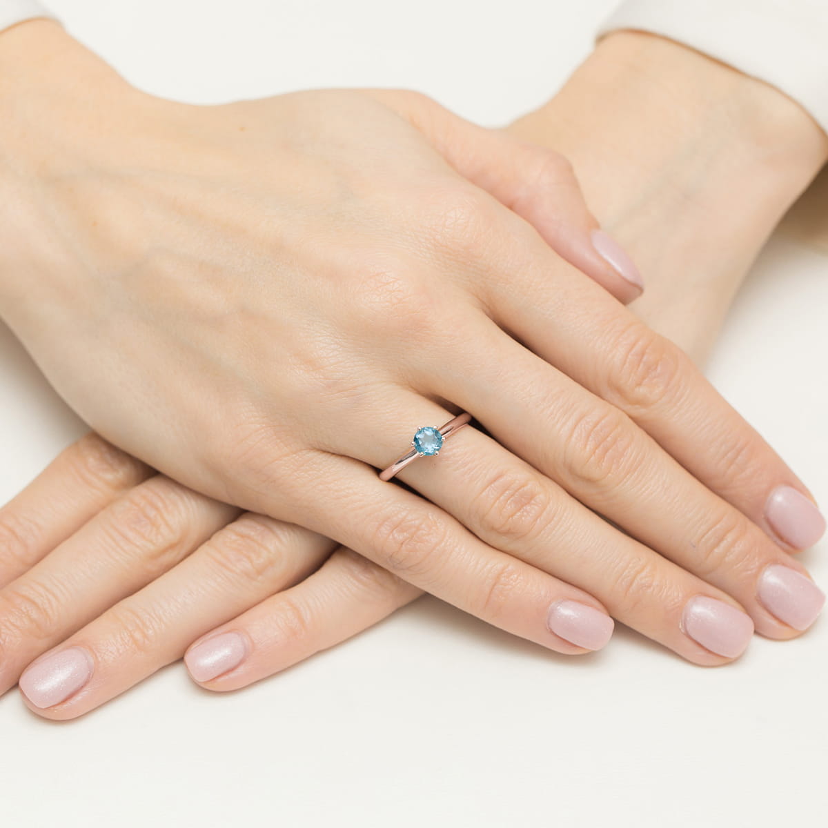 W0557.R3.TOB.01_4 Dwie ręce z delikatnym manicurem, na jednej z nich srebrny pierścionek z niebieskim kamieniem.
