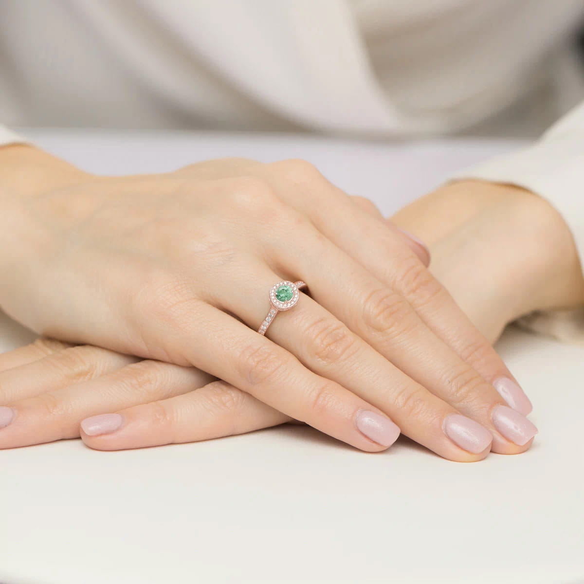 W0559.R3.EMG.01_4 Na dłoni z delikatnym manicure znajduje się pierścionek z zielonym kamieniem otoczonym diamentami.