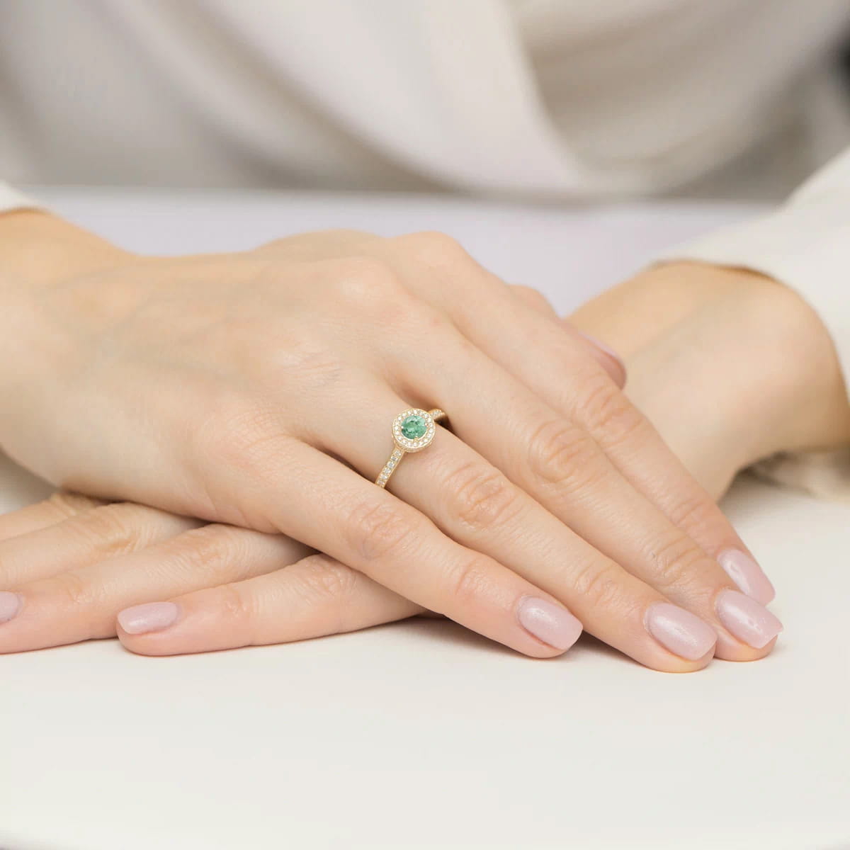 W0559.Z3.EMG.01_4 Złoty pierścionek z zielonym kamieniem na dłoni z delikatnym manicure.
