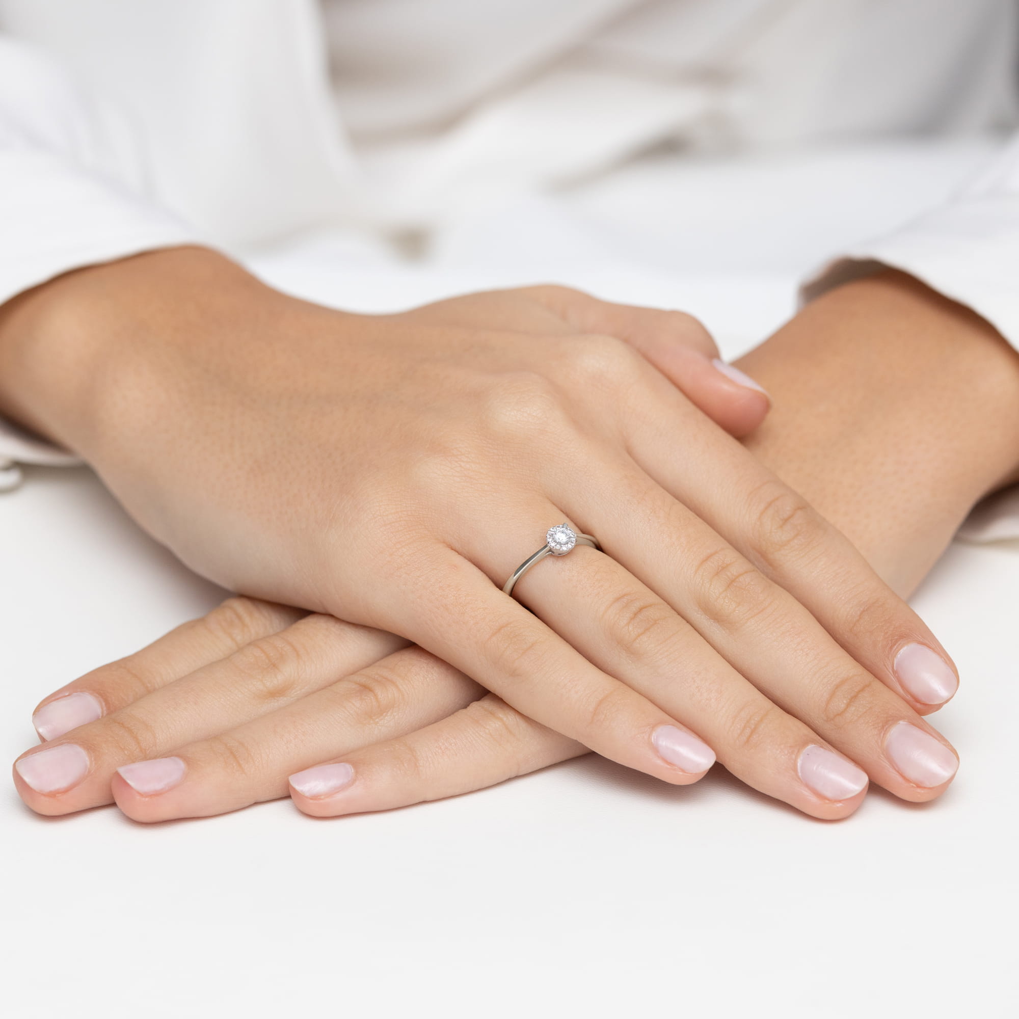 W0560.B3.DIW.01_4 Na dłoniach kobiety znajduje się delikatny pierścionek z diamentem, a paznokcie są starannie pomalowane na jasny kolor.