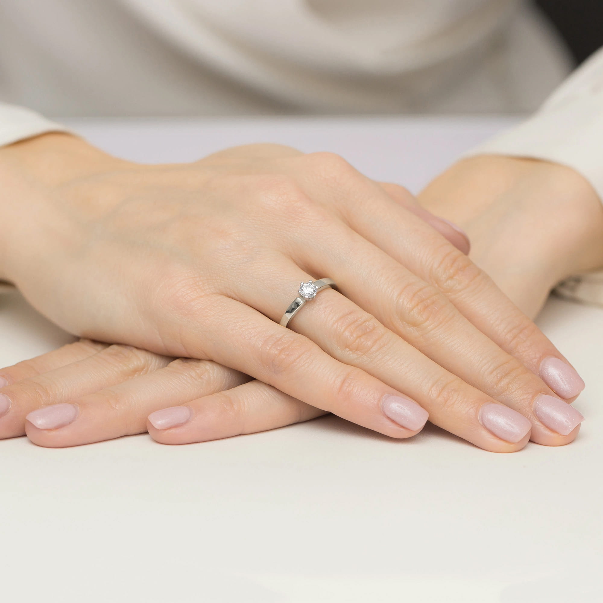 W0562.B3.DIW.01_4 Dwie ręce z delikatnym manicure, jedna z pierścionkiem z diamentem na palcu.