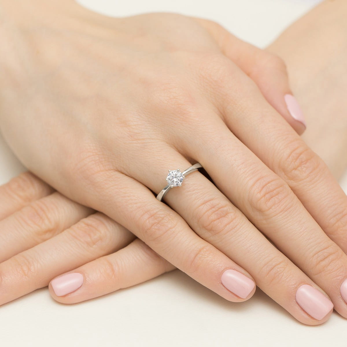 W0563.B3.LDW.02_4 Dwie dłonie z delikatnym manicure, na jednej z nich błyszczący pierścionek z dużym diamentem.