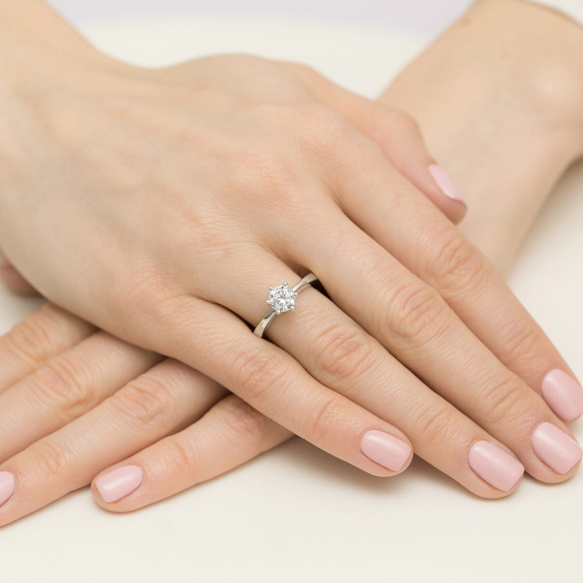 W0563.B3.LDW.03_4 Dwie ręce z delikatnym manicurem, jedna z pierścionkiem z dużym diamentem na srebrnej obrączce.