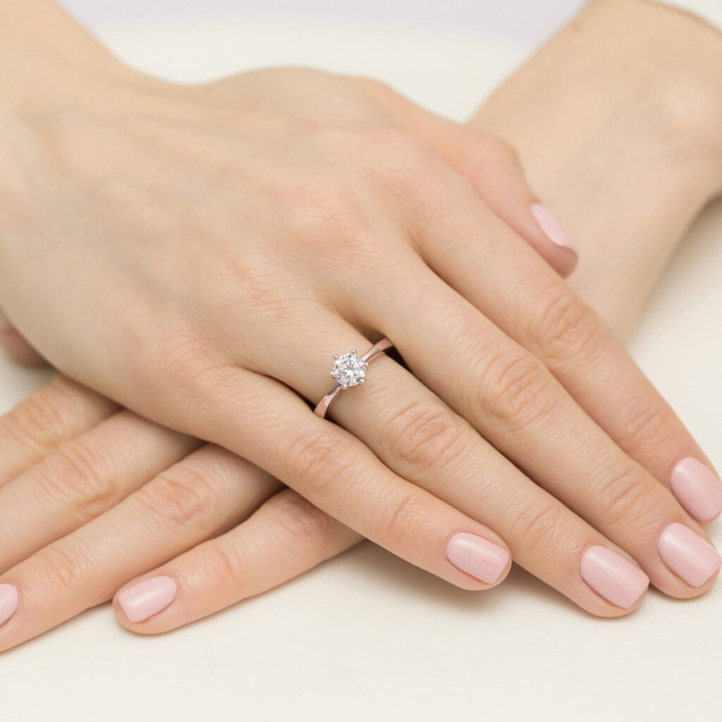 Na dłoni z różowym manicure znajduje się pierścionek z dużym diamentem.