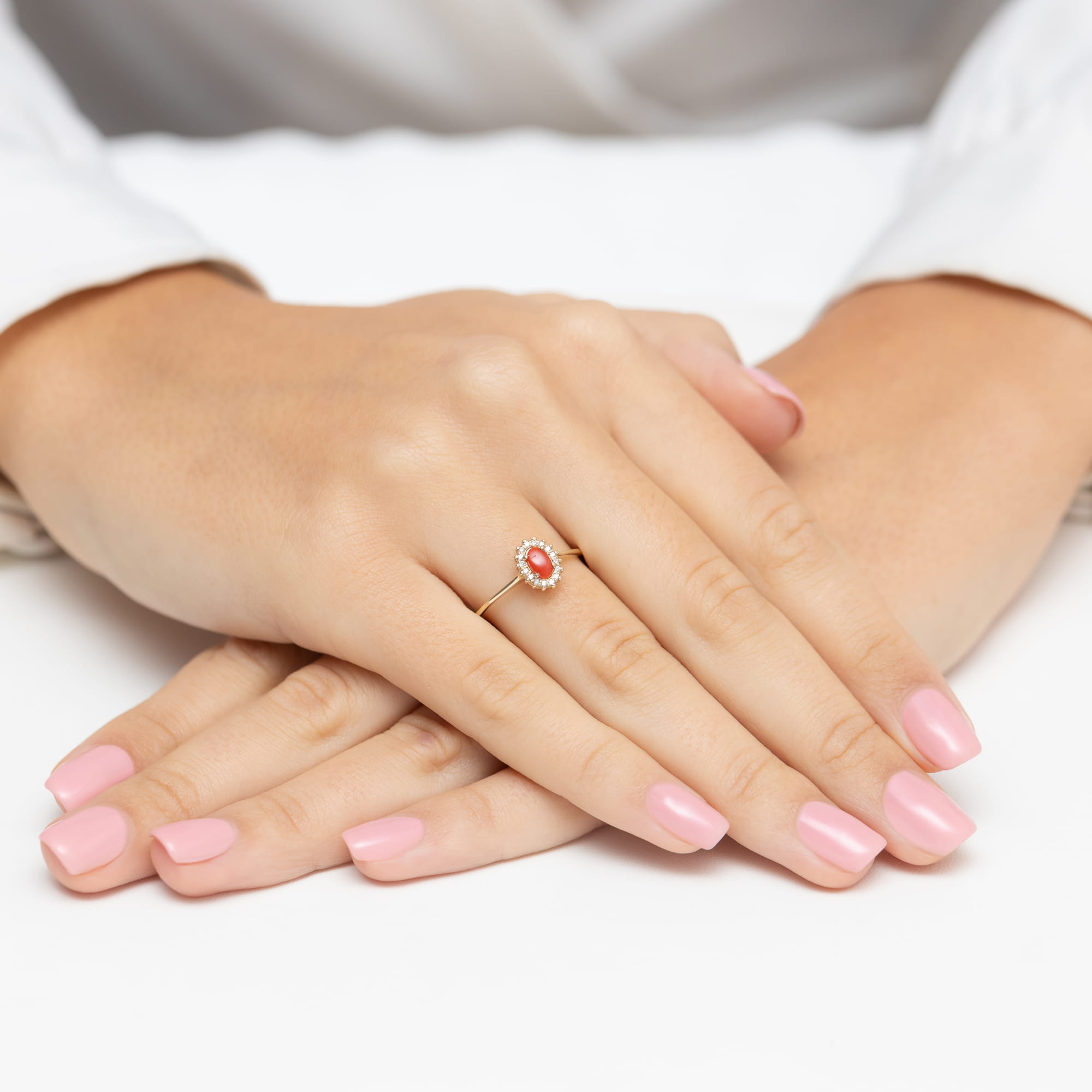 W0569.Z3.COR.01_4 Ręce z różowym manicure, na jednym palcu pierścionek z czerwonym kamieniem otoczonym diamentami.