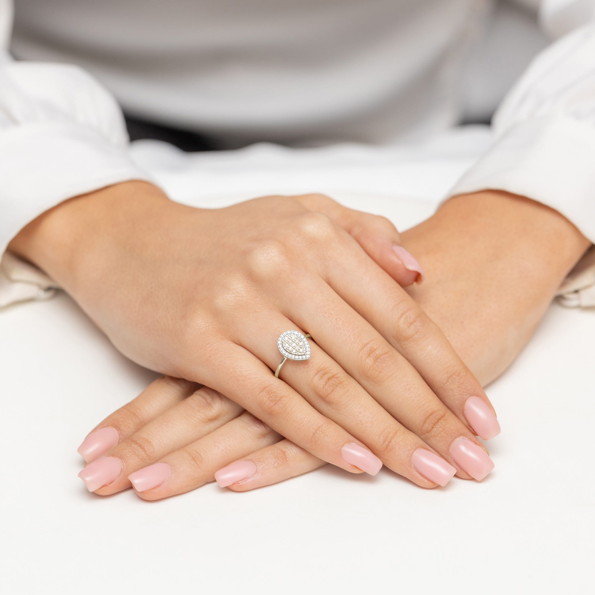 W0571.B3.DIW.01_4 Dwie dłonie z delikatnym manicure, jedna z pierścionkiem w kształcie łzy z diamentami.