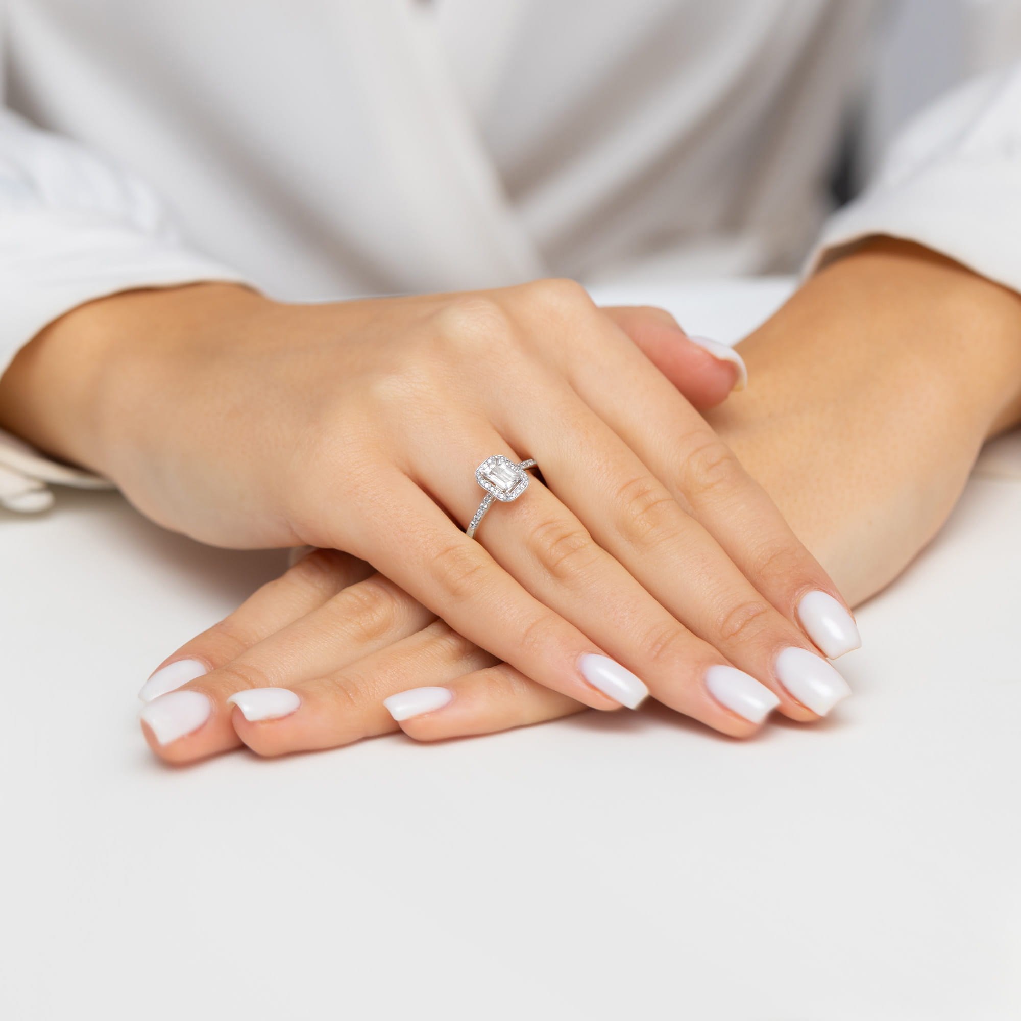 W0575.B3.LDW.01_4 Dwie dłonie z białym manicure, jedna z pierścionkiem z dużym diamentem na cienkiej obrączce.