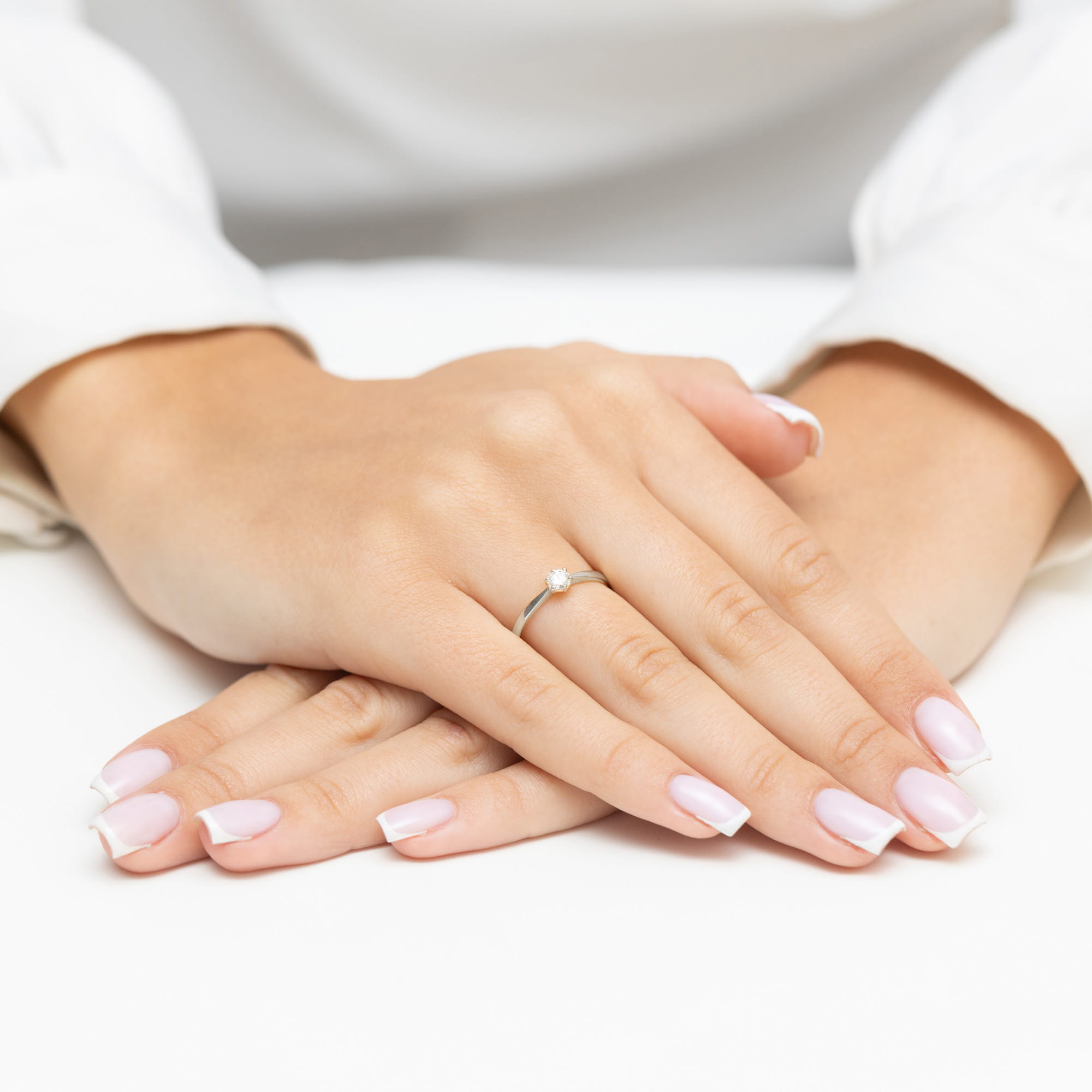 W0579.B3.DIW.03_4 Dwie dłonie z delikatnym pierścionkiem i zadbanymi paznokciami w jasnym kolorze.