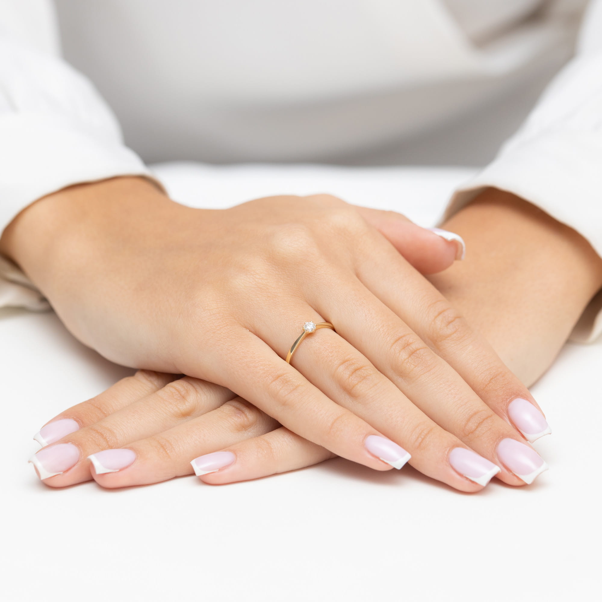 W0579.Z3.DIW.02_4 Dwie dłonie z delikatnym pierścionkiem na palcu, z zadbanymi paznokciami w jasnym kolorze.