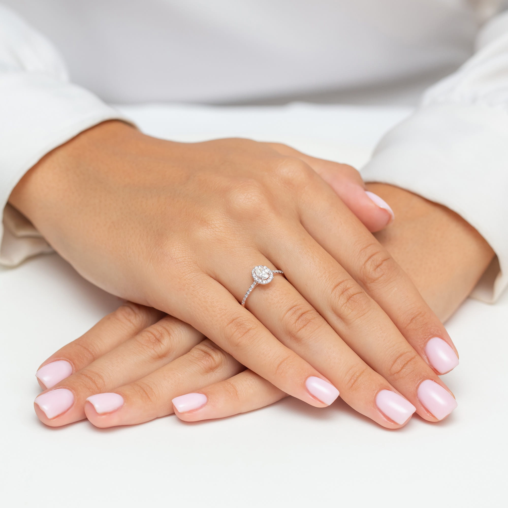 W0584.R3.DIW.01_4 Dwie dłonie z delikatnym pierścionkiem i różowym manicure, ułożone na białym tle.