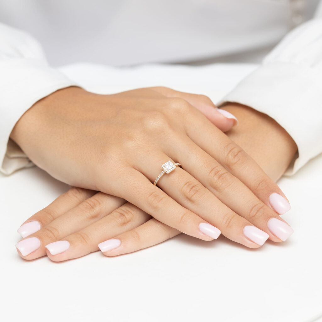 Dwie dłonie z delikatnym manicure w jasnym kolorze, jedna z pierścionkiem z diamentem.