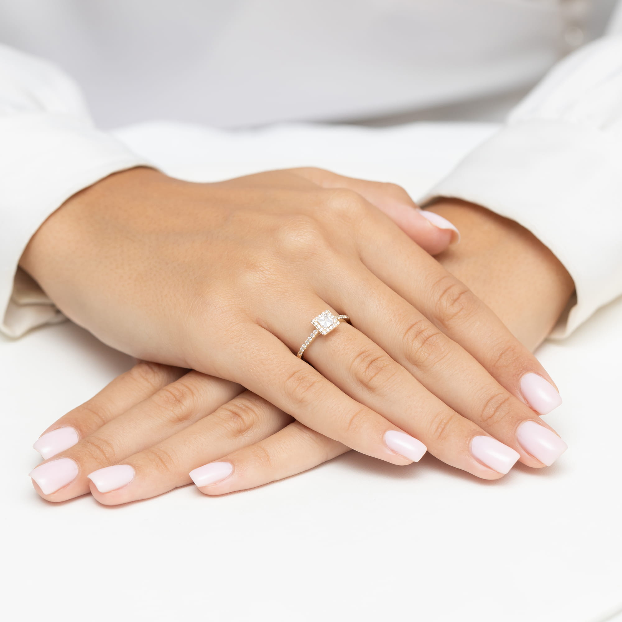 W0591.Z3.DIW.01_4 Dwie dłonie z delikatnym manicure w jasnym kolorze, jedna z pierścionkiem z diamentem.