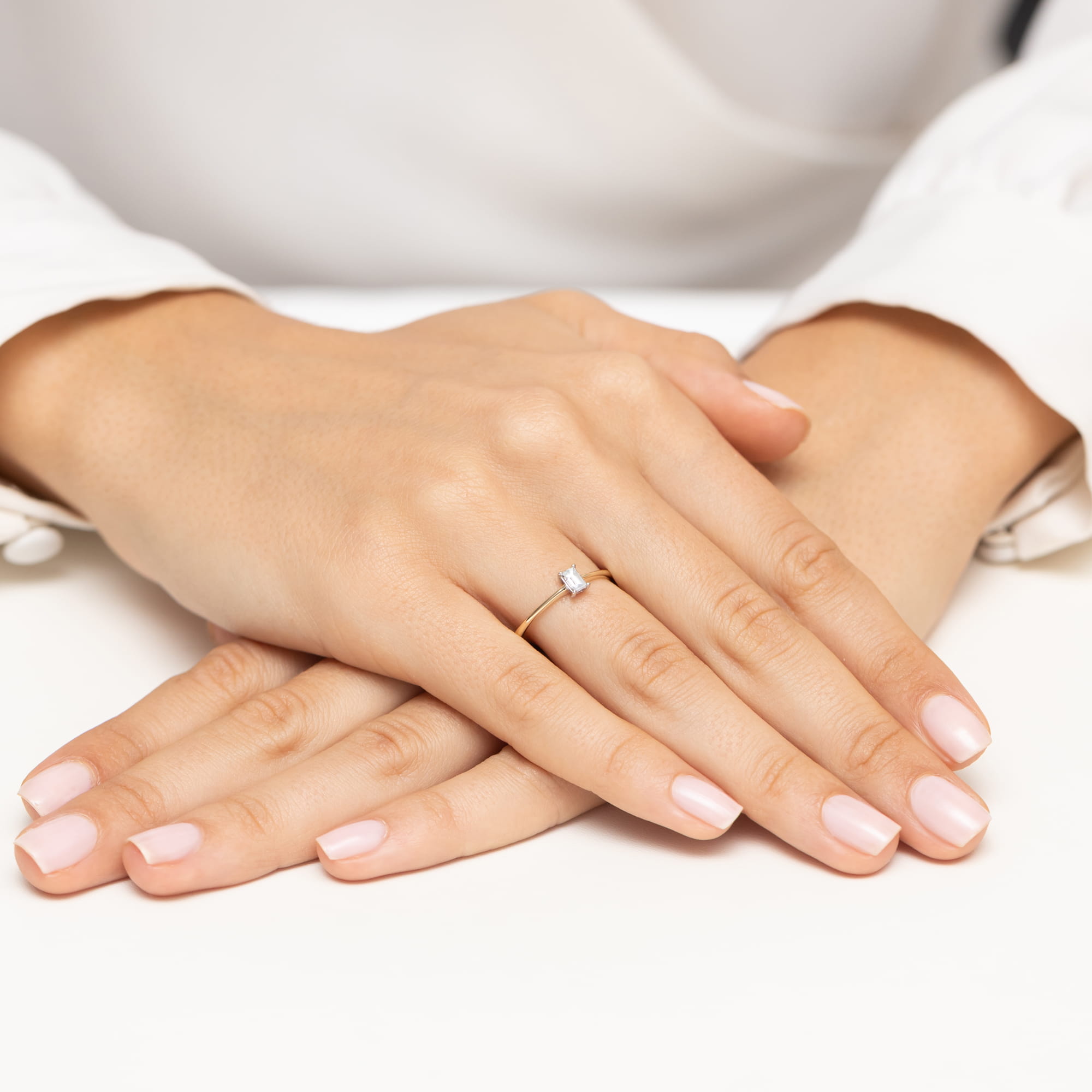 W0592.Z3.DIW.01_6 Zbliżenie na dłonie z delikatnym pierścionkiem na palcu, z zadbanymi paznokciami w jasnym kolorze.