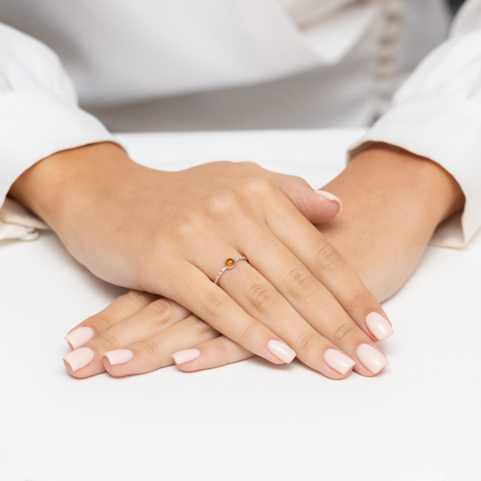 W0596.R3.TMY.01_4 Na dłoni z delikatnym manicure znajduje się srebrny pierścionek z pomarańczowym kamieniem.